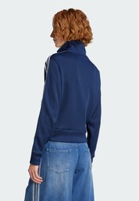 Marineblauer, gerippter Pullover mit hohem Kragen und weißen Seitenstreifen. Kombiniert mit hellblauen, weiten Denim-Hosen mit Gesäßtaschen.