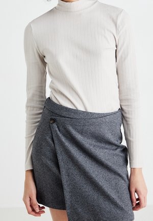 Personne portant un pull léger à col roulé côtelé et une jupe portefeuille grise à motif chevrons avec un détail de bouton.