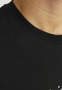 Sort bomulds t-shirt med rund hals, glat tekstur og korte ærmer. Bemærkelsesværdig trykdetalje ved kanten i lys farve.