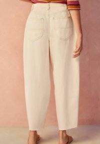 Ljust beige högmidjade vida jeans med två bakfickor och trasig nederkant. Bomullstyg med synliga sömdekorationer.
