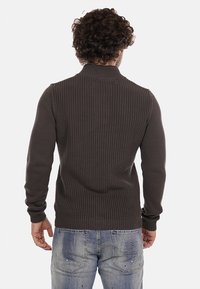 Maglione a coste di un grigio scuro, con colletto alto, silhouette aderente e maniche lunghe, abbinato a jeans blu sbiaditi.