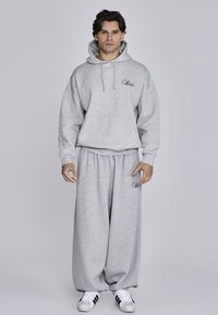 Graues Hoodie mit Kordelzügen und Fronttasche, dazu passende übergroße graue Jogginghose. Weicher Stoff mit minimalem gesticktem Detail.
