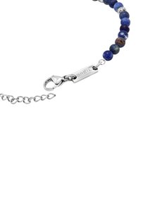 Pärlarmband med mörkblå och lila stenar, silverfäste och en metalltagg graverad med "BREIL." Kedjeutvidgning ingår.