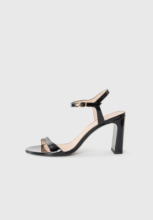 Schwarze lackledersandalen mit hohen Absätzen und einem Knöchelriemen, offener Zehenpartie und eckigem Absatz. Glatte Textur und minimalistisches Design.
