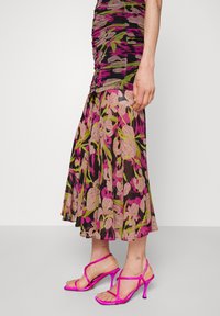 Floral dress with ruched bodice, featuring pink and green patterns on a black background. Paired with strappy pink heels with a tapered heel.