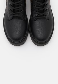 Stivali in pelle nera con finitura testurizzata, dotati di lacci neri e una robusta suola in gomma. Accenti laterali con motivo leopardato.