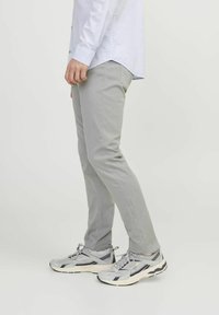 Světlé šedé slim-fit chinos s hladkou texturou, doplněné šedými a černými sportovními botami s prodyšnými detaily a bílou podrážkou.