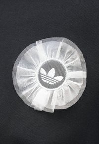 Μαύρο ύφασμα διαθέτει ένα κυκλικό λευκό δίχτυ σε σχήμα λουλουδιού με ένα λογότυπο τριών ριγωμάτων σε στρογγυλή βάση στο κέντρο.