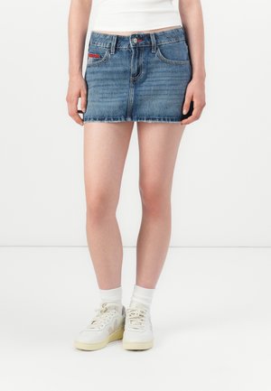 Denim mini skjørt i lys blå med utslitt kant, med to frontlommer, subtil søm, og en liten rød merkevarelogo på lommen.