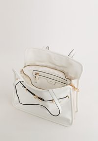Hvid læderhåndtaske med hardware i guldfarve, en lynlåslomme indeni og kontrasterende sort syning langs kanterne. Åben design.