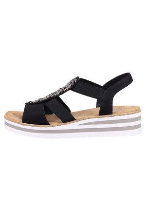 Sandale noire avec des brides élastiques, des accents décoratifs en argent, une semelle intérieure rembourrée et une semelle compensée rayée en blanc et gris.