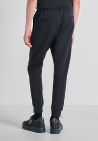 Marine joggingshorts gemaakt van zachte stof met een elastische tailleband, met twee achterzakken en taps toelopende boorden. Draagt zwarte sneakers.