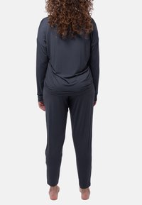 Maglietta grigia a maniche lunghe e pantaloni abbinati realizzati in tessuto liscio, con una vestibilità comoda e dettagli di vita arricciata, visti da dietro.
