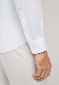 Witte linnen blouse met lange mouwen en knopenmanchetten, met een zachte textuur en subtiele glans, gecombineerd met lichtgekleurde, gestructureerde broek.