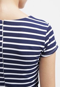 Navy ja valge triibuline tipp lühikeste varrukatega, millel on tagumine lukk ja sile, veniv kangas. Lihtne ümmargune kaelusdisain.