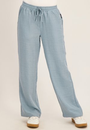Lichtblauwe broek met wijde pijpen en een elastische tailleband met koord, gedragen met witte sneakers tegen een neutrale achtergrond.