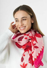 Écharpe florale présentant des teintes rouges et roses, avec des motifs audacieux de feuilles et de fleurs. Tissu léger tombant autour du cou.