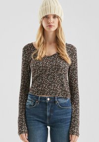Langarm bloemen blouse met een diepe V-hals, zwarte achtergrond en patronen van kleine roze, witte en gele bloemen; gecombineerd met blauwe jeans.
