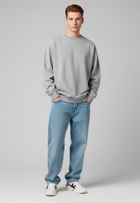 Felpa grigia chiaro con scollo rotondo, abbinata a jeans azzurri chiaro. Sneakers bianche con dettagli neri completano l'outfit.