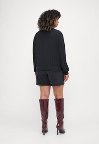 Black bomber jacket with ribbed cuffs, worn over dark shorts, paired with glossy burgundy knee-high boots. Smooth texture, casual design.