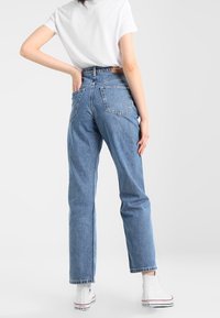 Högmidjade blå denimjeans med rak ben, bakfickor och fransad fåll, bärs med vita högskor.