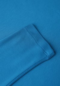 Niebieska koszula z długim rękawem, charakteryzująca się gładką teksturą materiału, okrągłym wykończeniem mankietów oraz widocznymi detalami przeszycia.