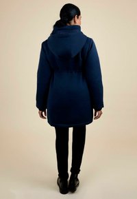 Cappotto imbottito blu navy con cappuccio, caratterizzato da un elastico in vita, maniche lunghe e orlo curvato, abbinato a pantaloni neri.