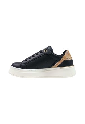 Sneaker nera low-top con suola bianca spessa, chiusura con lacci frontale e dettaglio sul tallone beige con motivo e particolare metallico.