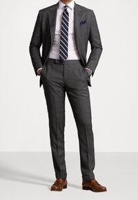 Szary garnitur z klapą typu notch, biała koszula, niebiesko-biała wąska krawat, poszetka w kropki i brązowe skórzane buty.