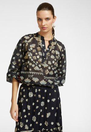 Blusa nera con motivo floreale, maniche lunghe arrotolate e scollatura a V, abbinata a una gonna coordinata con un motivo simile.