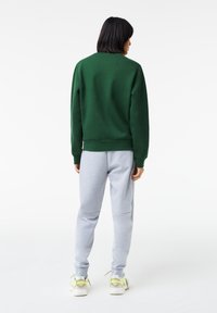 Grøn sweatshirt parret med grå sweatpants. Sweatshirten har en rund hals og ribbede manchetter, mens bukserne har en afslappet pasform.