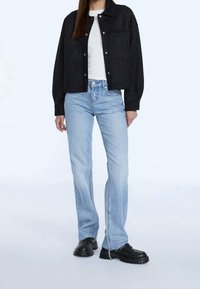 Giacca corta in suede nera con bottoni a pressione sopra un top bianco a coste; jeans svasati azzurri chiari; scarpe nere chunky con suole testurizzate.