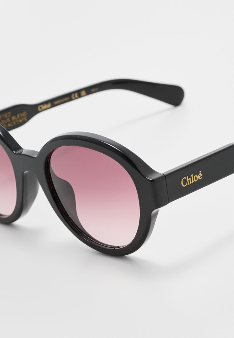 Schwarze Sonnenbrille mit übergroßen ovalen Fassungen, gradienten rosa Gläsern und goldener "Chloé"-Markierung an den Bügeln. Glatte, glänzende Oberfläche.