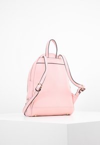 Růžový kožený batoh s texturovaným povrchem, dvojitými nastavitelnými popruhy, zlatými kovovými doplňky a kontrastním černým lemem.