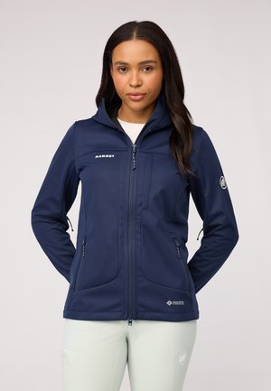 Chaqueta softshell navy con cierre frontal, dos bolsillos laterales y un cuello alto. Presenta un logo en el pecho y el hombro. Textura suave.