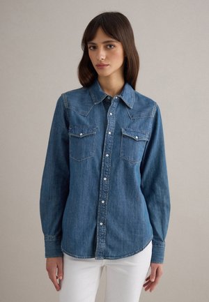 Blauw denim overhemd met lange mouwen, een puntige kraag, twee borstzakken en een knopenrij aan de voorkant. Voorzien van een gebogen zoom en lichte stiksel details.