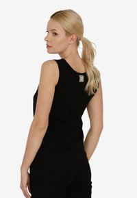 Blondynka z kucykiem, ubrana w czarny bezrękawnik z prążków i pasujące spodnie, odwrócona lekko w bok, żeby pokazać detale pleców.