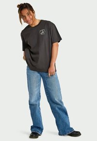 T-shirt in cotone nero con maniche corte e collo rotondo, caratterizzato da una stampa grafica bianca. Abbinato a jeans blu e stivali neri.