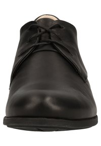 Chaussure lacée en cuir noir avec une texture lisse, un bout rond et un design minimaliste. Dotée d'une semelle en caoutchouc plate et de lacets ton sur ton.