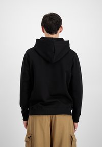Zwarte hoodie met een capuchon, geribbelde manchetten en zoom, getoond vanuit de achterkant, gecombineerd met khaki cargobroek. Eenvoudig ontwerp en zachte textuur.
