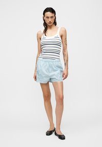 Ριγέ αμάνικο τοπ σε λευκό και ναυτικό μπλε, συνδυασμένο με ανοιχτόχρωμο μπλε σορτς με κεντήματα λουλουδιών, σε στυλ με μαύρες φλατ παπούτσια.