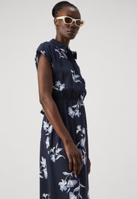 Abito floreale navy con maniche corte, chiusura frontale a bottoni e vita elastica. Presenta fiori azzurri su un tessuto morbido e fluido.