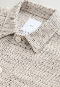 Light beige shirt with a textured striped pattern, featuring a collared neckline and a button closure. Label visible inside.