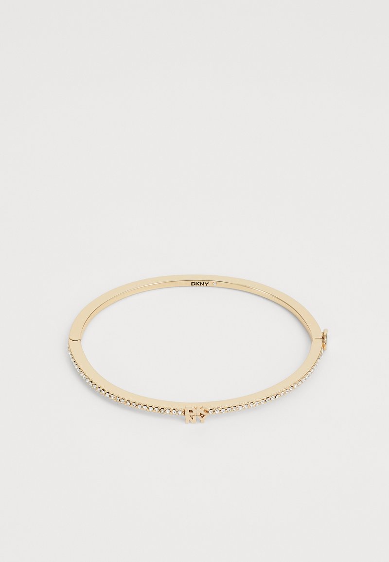 Bracciale a bangle in tonalità oro con una finitura liscia, impreziosito da strass trasparenti lungo un lato e una chiusura a gancio. Logo visibile all'interno.