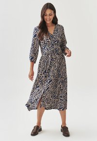 Vestido azul marino con un estampado de hojas en beige, escote en V, detalles de botones, mangas de tres cuartos y una abertura lateral, hecho de una tela ligera.