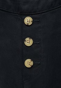 Črn material z teksturirano površino, ki ima štiri kremne gumbe, vsak s tortoiseshell vzorcem in petimi luknjami.