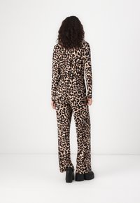 Mono de leopardo de manga larga, con cinturilla elástica y pantalones de pernera ancha. La tela presenta una textura suave y lisa. Zapatos de plataforma negros.