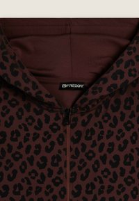 Hoodie zippé marron avec imprimé léopard noir, fabriqué en tissu doux. Comprend une capuche et une étiquette de marque au niveau du col.