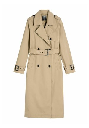 Beżowy długi płaszcz trencz z podwójnym rzędem czarnych guzików, paskiem w talii i mankietach, szerokimi klapami oraz pagonami na ramionach.