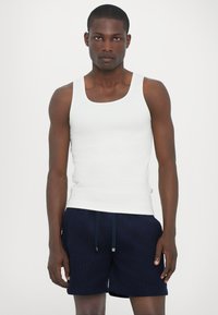 Débardeur en coton blanc avec un col rond, associé à un short bleu marine avec un cordon de serrage et des poches latérales. Design simple, coupe régulière.